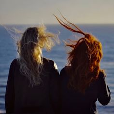 two women with long hair looking out at the ocean