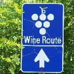 a blue sign that says wine route and an arrow pointing to the left with trees in the background