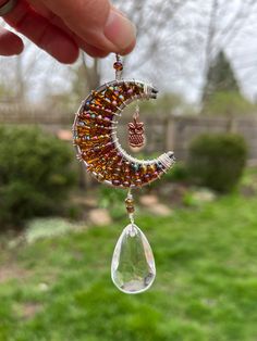 a person is holding up a beaded crescent and tear droplet