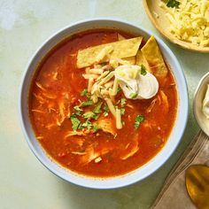 a bowl of soup with tortilla chips and sour cream on the side next to it