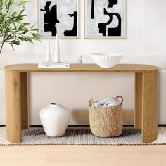 two black and white paintings on the wall above a wooden table with baskets underneath it