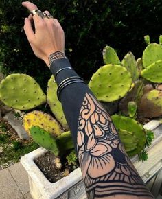 a person's arm with tattoos on it next to some cactuses and plants