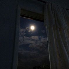 the full moon is seen through an open window in a dark room with white curtains