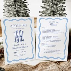 two blue and white wedding stationery cards sitting on top of a table next to a pine tree