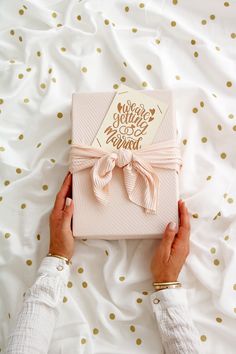 two hands holding a pink gift box with a gold foil lettering on it that says happy new year