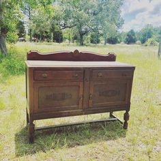 an old wooden dresser sitting in the middle of a field with grass and trees behind it