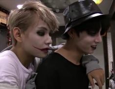 two young men with makeup on their faces and one is wearing a fedora hat