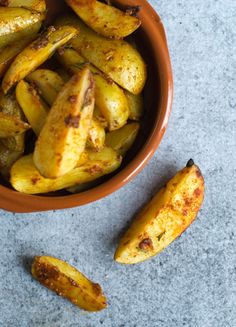 a brown bowl filled with fried potatoes on top of a gray counter next to a knife