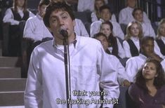 a man singing into a microphone in front of a group of people with white shirts