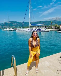 a woman in a yellow skirt standing on a dock next to the water and boats