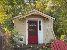 a small shed with a red door and two adiron chairs in front of it