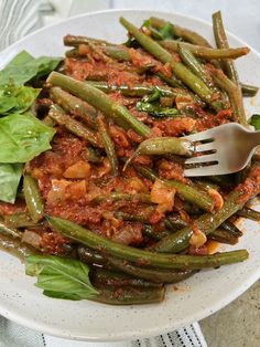 a white plate topped with green beans covered in sauce and lettuce next to a fork