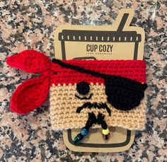 a crocheted cup cozy with a pirate hat and eye patch on it's side