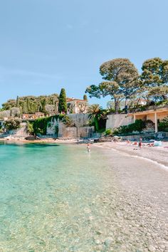 people are on the beach and in the water near some buildings with trees around them