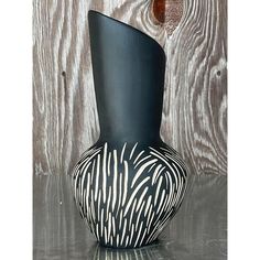 a black and white vase sitting on top of a table next to a wooden wall