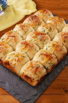 bread with cheese and herbs is on a slate platter next to a yellow towel