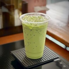 a plastic cup filled with green liquid sitting on top of a black tray next to a wooden table