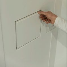 a person is holding the door handle on a white cabinet with a square shaped opening