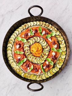 a pizza with cucumbers and tomatoes in a pan on a marble counter top