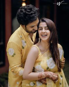 a man and woman standing next to each other in front of a building with flowers on it