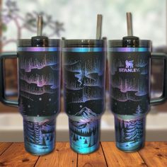 three travel mugs sitting on top of a wooden table