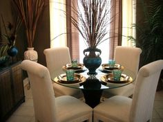 a glass table with white chairs around it and a vase on the top of it