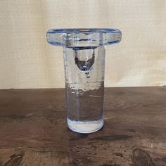 a clear glass with water in it sitting on a wooden table next to a wall