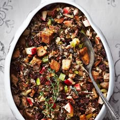 a white dish filled with stuffing and vegetables next to a spoon on a tablecloth