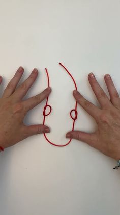 two hands with red string on white surface next to each other and one hand holding the string