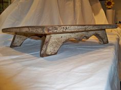 an old wooden bench sitting on top of a white tablecloth covered bedspread