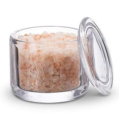 a glass container filled with sea salt on top of a white table next to a lid