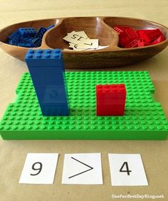 a lego table with two matching numbers and a wooden bowl full of colored plastic blocks