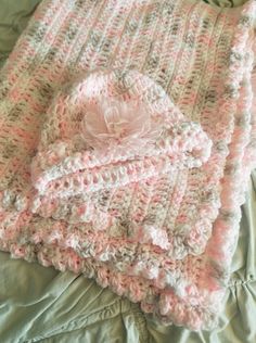 two blankets laying on top of each other on a green bed cover with pink and white crocheted designs