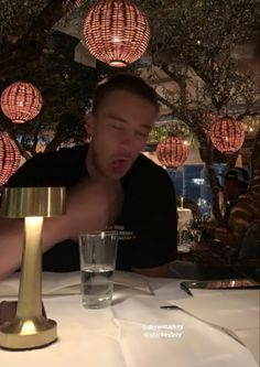 a man sitting at a table with a glass in front of him and lights hanging from the ceiling