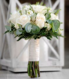 a bridal bouquet with white roses and greenery in a vase on a table