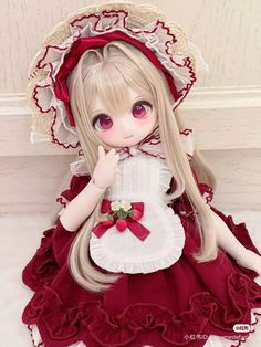 a doll with long blonde hair wearing a red dress and bonnet sitting on the floor