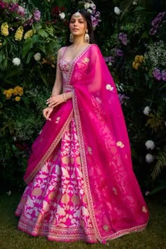 a woman in a pink and gold lehenga standing next to flowers with her hands on her hips