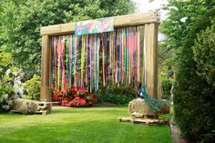 an outdoor area with grass, flowers and wooden structures made out of strips of colored streamers