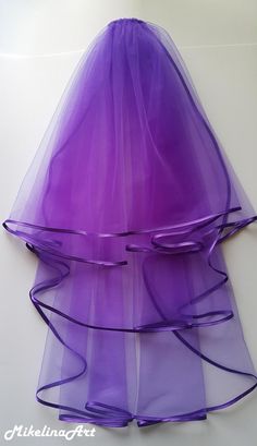 a purple veil is sitting on top of a white surface with blue ribbon around it