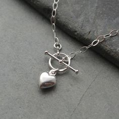 "This sterling silver necklace features a sterling silver heart charm and has a T bar clasp for front fastening It is made from flat oval sterling silver trace chain The sterling silver filled heart charm is hollow and measures 10 mm. The t-bar measures 18 mm with the ring having a 10 mm outside diameter Available in  a choice of 14\", 15\", 16, 18  or 20 inch sterling silver chain. A Lovely everyday wear necklace. Lovely gift for a loved one. The necklace will arrive in a gift box." Sterling Silver Heart Necklace With Toggle Clasp, Heart Shaped Sterling Silver Necklace With Toggle Clasp, Silver Heart Toggle Necklace For Gift, Silver Heart Toggle Necklace As Gift, Silver Heart Toggle Necklace With Charm, Silver Heart Toggle Necklace With Heart Charm, Silver Toggle Necklace With Heart Charm, Silver Heart Necklace With Toggle Clasp For Gift, Silver Heart Charm Toggle Necklace For Valentine's Day