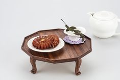 a small wooden tray with some food on it next to a teapot and cup