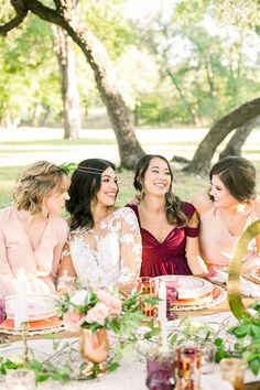 four women sitting at a table with plates and drinks in front of them, laughing