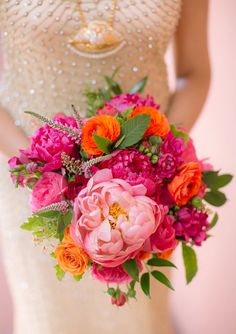 a bride holding a bouquet of pink and orange flowers on her wedding day in front of a wall