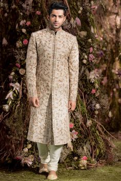 a man standing in front of a flower covered wall wearing a beige sherve