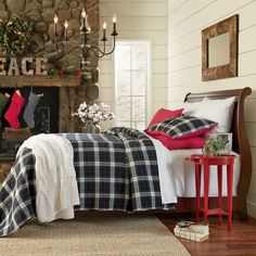 a bedroom decorated for christmas with plaid bedding and blankets on the bed, fireplace in the background