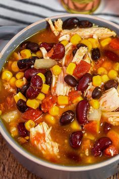 a bowl filled with chicken, beans and corn soup on top of a wooden table