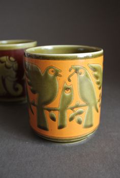 two cups with birds painted on them sitting next to each other in front of a gray background