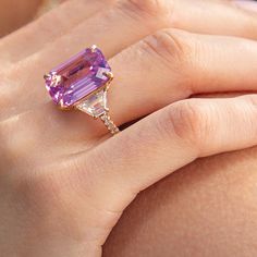 a close up of a person's hand holding an amethorate and diamond ring