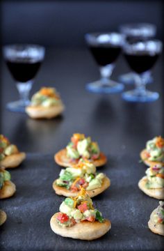 small appetizers are lined up on a black surface with wine glasses in the background