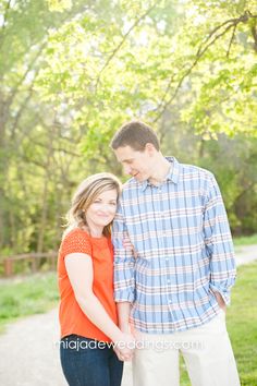 a man and woman standing next to each other on a path in front of trees